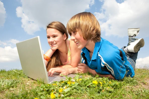 Två leende tonåringar med laptop vilar på ängen. — Stockfoto