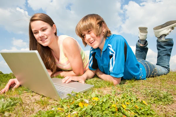 Dos adolescentes sonrientes con portátil descansando en el prado . — Foto de Stock
