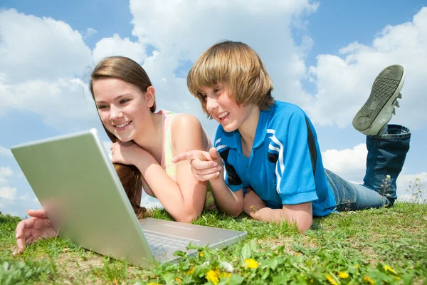 Dos adolescentes sonrientes con portátil descansando en el prado . — Foto de Stock
