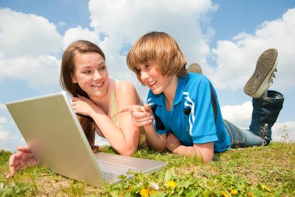 Twee lachende tieners met laptop rusten op weide. — Stockfoto