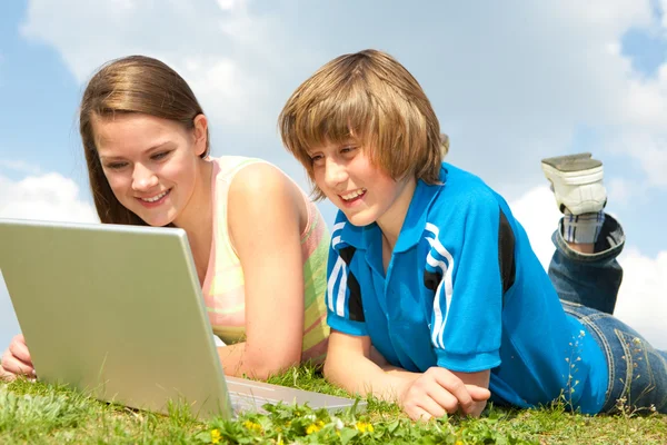 Twee lachende tieners met laptop rusten op weide. — Stockfoto