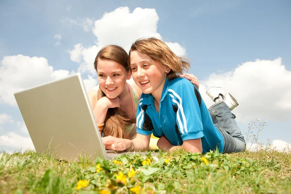 Dois adolescentes sorridentes com laptop descansando no prado . — Fotografia de Stock