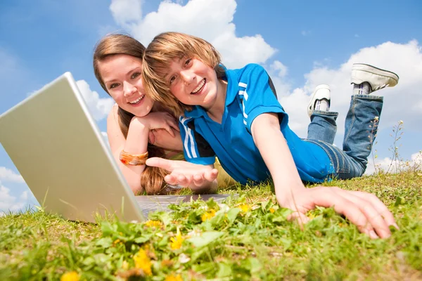 两个微笑少年与笔记本电脑在草地上休息. — 图库照片