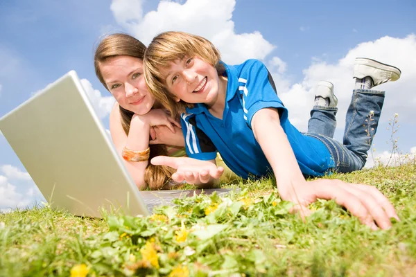 两个微笑少年与笔记本电脑在草地上休息 — 图库照片
