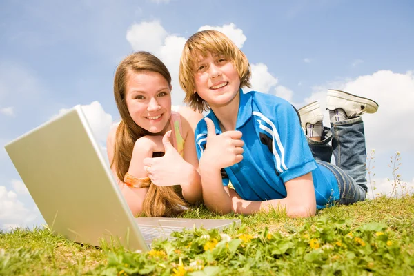 Deux adolescents souriants avec ordinateur portable reposant sur la prairie . — Photo