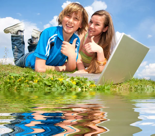 Deux adolescents souriants avec un ordinateur portable reposant sur la prairie. Réfléchi i — Photo