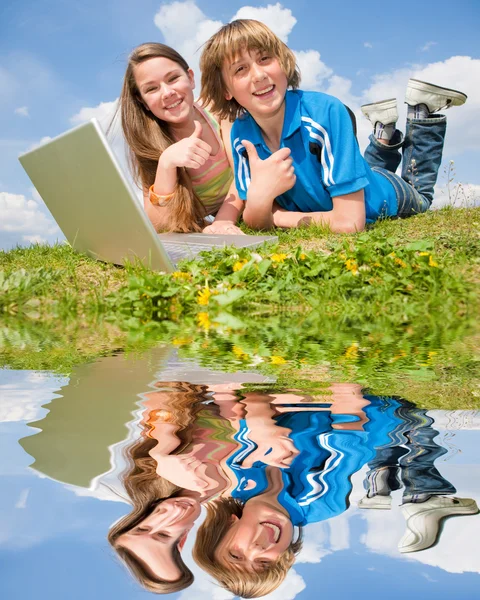 Двоє усміхнених підлітків з ноутбуком відпочивають на лузі. Відбитий i — стокове фото