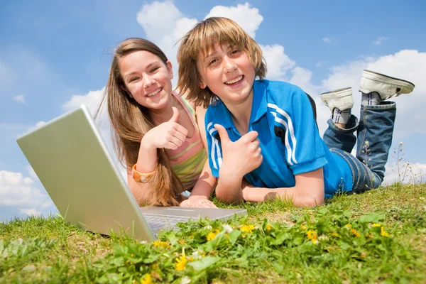 两个微笑少年与笔记本电脑在草地上休息 — 图库照片