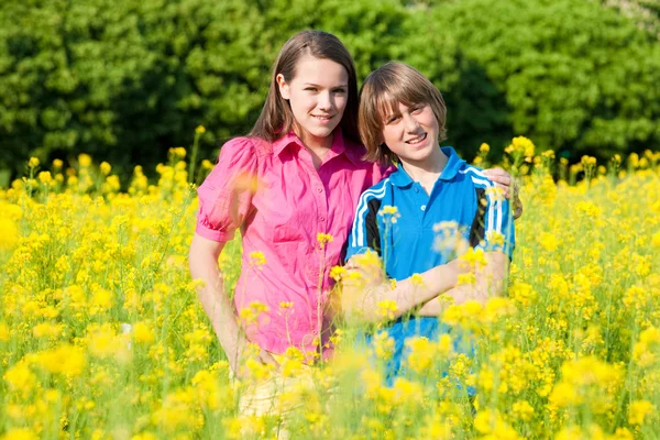 Flicka och pojke avkopplande på äng full av gula blommor. mjuk foc — Stockfoto