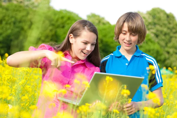 Two Smiling Teenagers Laptop Meadow Full Yellow Flowers Soft Focus — Stock Photo, Image