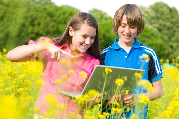 Dos adolescentes sonrientes con portátil en el prado . — Foto de Stock