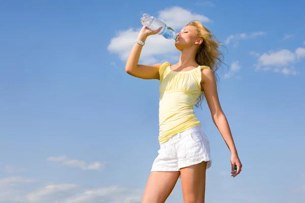 Красивая девушка пьет воду на фоне голубого неба — стоковое фото