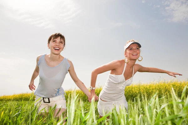 Duas jovens felizes estão correndo em um campo — Fotografia de Stock