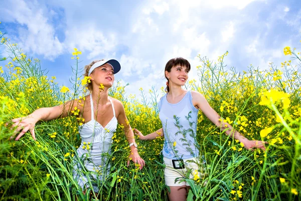 Two beautiful girl in white clothes go to the yellow flowers — Stock Photo, Image