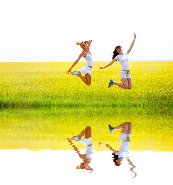 Two beautiful girl in white clothes jumps the yellow flowers — Stock Photo, Image