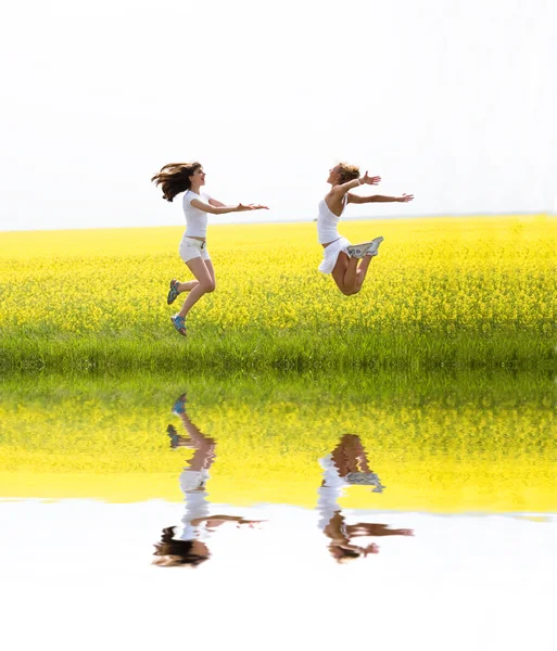 Twee mooi meisje in witte kleren springt de gele bloemen — Stockfoto