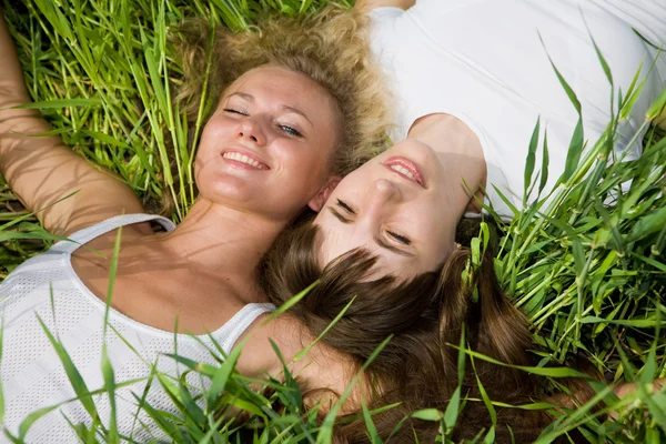 Two beautiful young women lay on green grass outdoors — Stock Photo, Image