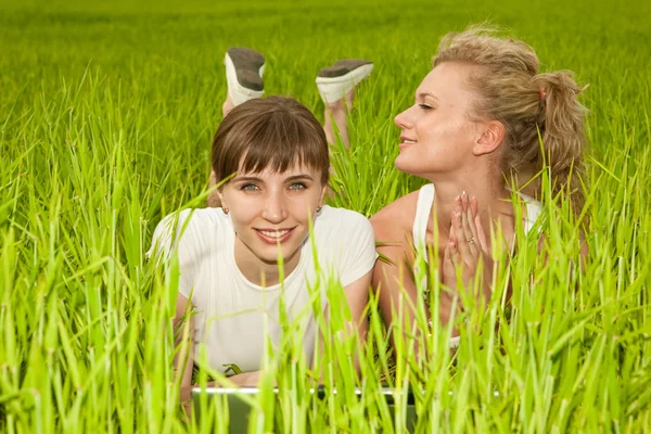 Dos hermosas chicas en ropa blanca se ríen de ordenador portátil comp —  Fotos de Stock