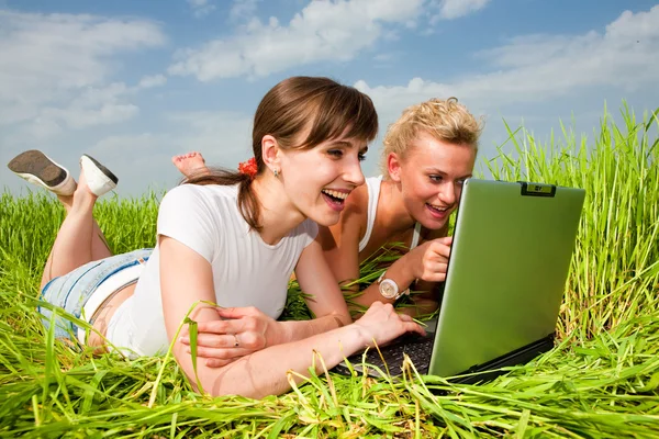白い服を着て つの美しい女の子は笑って 屋外のラップトップ コンピューターを見てします 緑の草に横たわっていた — ストック写真