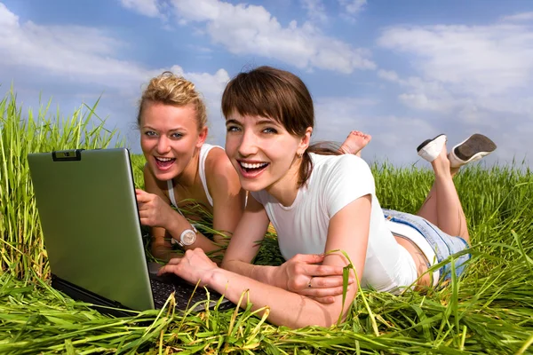 白い服を着て つの美しい女の子は屋外のラップトップ コンピューターの近くに笑っています 緑の草に横たわっていた — ストック写真