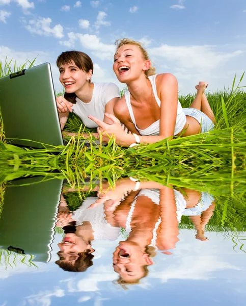 白い服を着て つの美しい女の子は笑って 屋外のラップトップ コンピューターを見てします 緑の草に横たわっていた — ストック写真