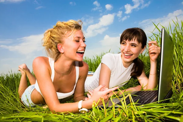 两个美丽的女孩在户外的便携式计算机上的白色衣服 躺在绿草地上 — 图库照片