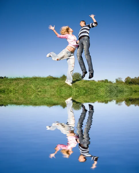 Šťastný mladý pár skákání na obloze nad zelenou louku — Stock fotografie