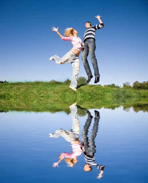 Happy young couple jumping in sky above a green meadow