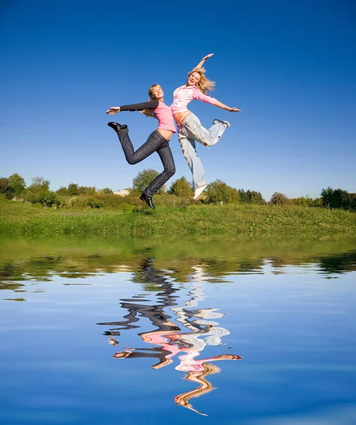 Duas meninas felizes pulando no prado verde . — Fotografia de Stock