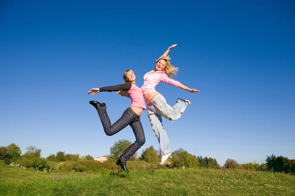 Due ragazze felici che saltano sul prato verde . — Foto Stock