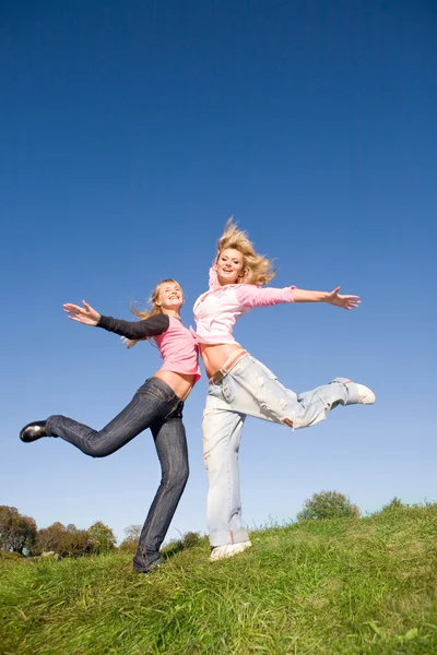 Dwie szczęśliwe dziewczyny skaczące na zielonej łące. — Zdjęcie stockowe