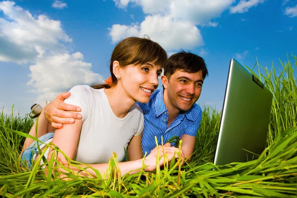 Casal casal feliz em um computador portátil ao ar livre. Deite-se no gr — Fotografia de Stock