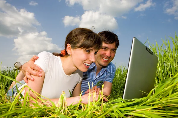 Happy couple on a laptop computer outdoors. Lay on the green gra — Stock Photo, Image