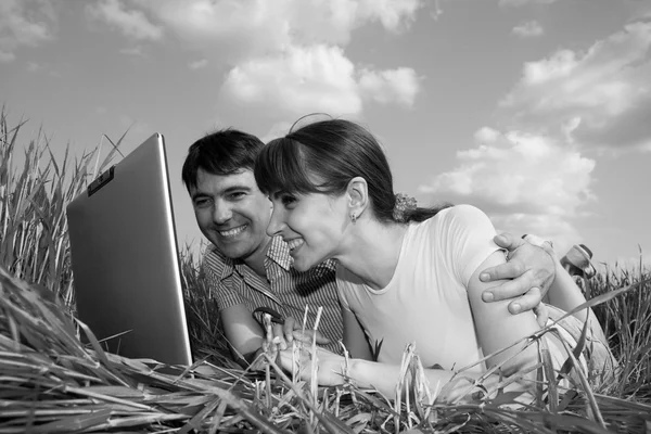 Casual casal feliz no computador portátil ao ar livre. Deite-se no gras — Fotografia de Stock