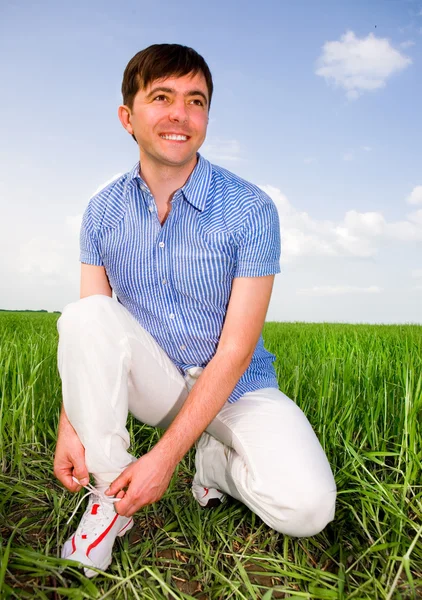 El hombre está atando cordones en un campo verde —  Fotos de Stock