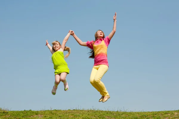 跳跃的绿草地上的两个女孩 — 图库照片
