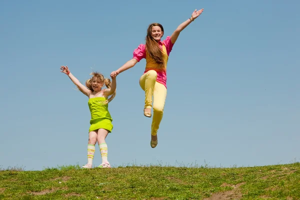 Two girls jumping on green meadow — Stock Photo, Image