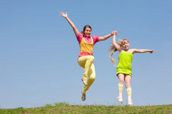 Duas meninas pulando no prado verde — Fotografia de Stock