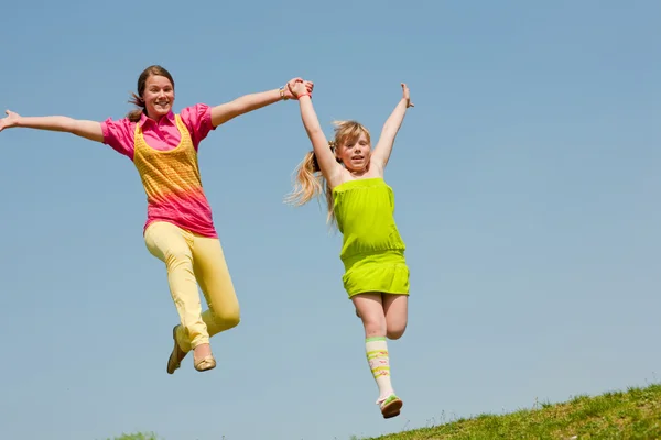 Iki kız yeşil çayır üzerinde atlama — Stok fotoğraf