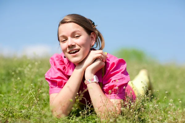 Досить усміхнена дівчина розслабляється на зеленому лузі, повній квітів. Отже — стокове фото
