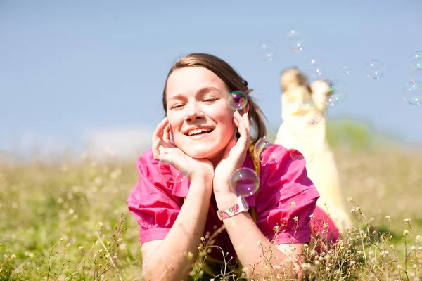Hübsches lächelndes Mädchen entspannt sich auf einer grünen Wiese voller Blumen. so — Stockfoto