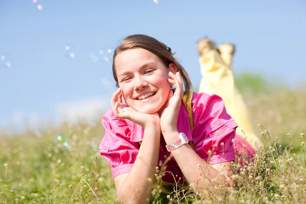 Красивая улыбающаяся девушка отдыхает на зеленом лугу, полном цветов. Итак... — стоковое фото