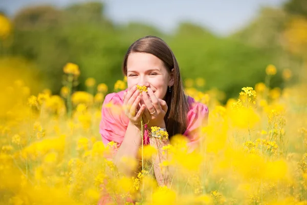 Досить усміхнена дівчина розслабляється на лузі, повній жовтих квітів. S-подібні — стокове фото