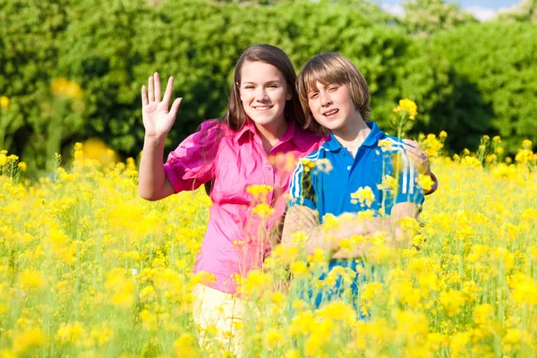女孩和男孩放松在草甸充满了黄色的花朵。软 foc — 图库照片