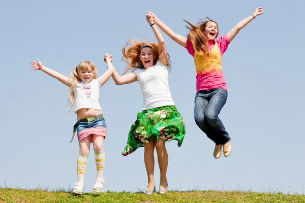快乐妈妈和跳跃的绿草地上的两个女儿 — 图库照片