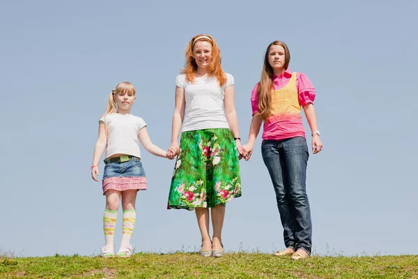 Mãe feliz e duas filhas pulando no prado verde — Fotografia de Stock