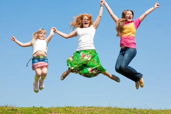 ハッピーママと緑の草原にジャンプ つの娘 — ストック写真