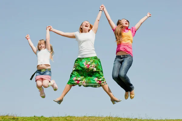 Mãe feliz e duas filhas pulando no prado verde — Fotografia de Stock