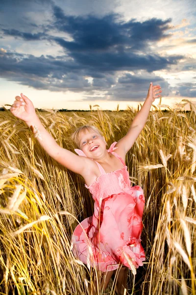 La niña salta en un campo de trigo. Contra el telón de fondo de s nublado — Foto de Stock