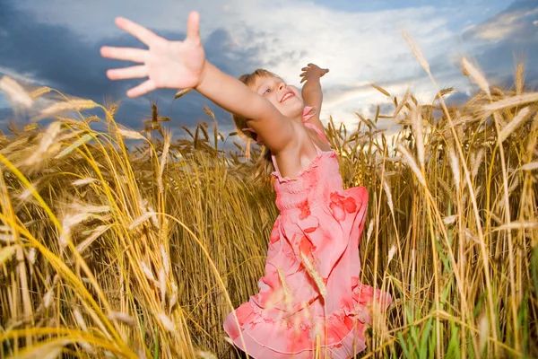 Little girl jumps in a wheat field. Against backdrop of cloudy s — Stock Photo, Image